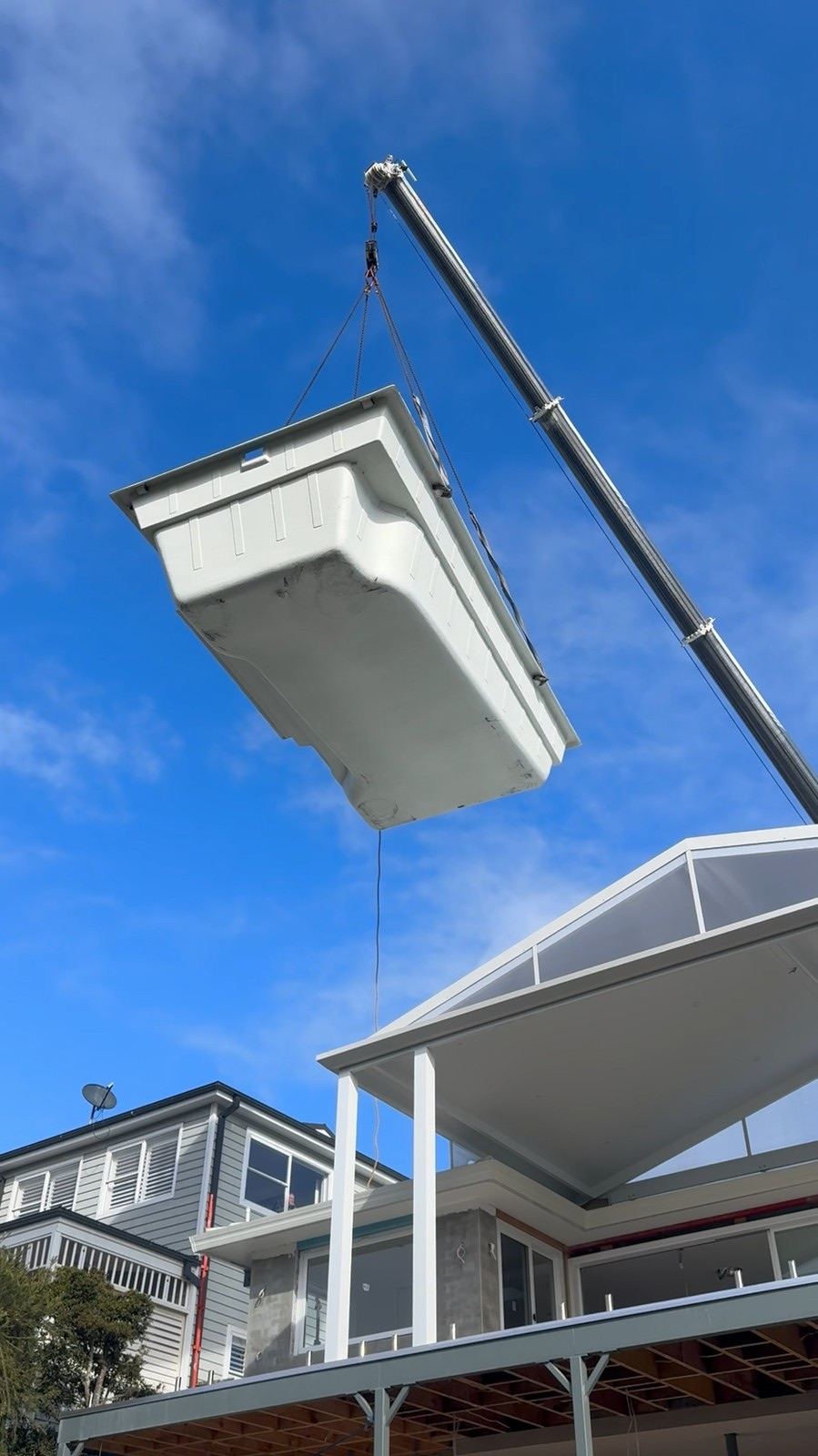 A fibreglass pool shell in the air on the crane